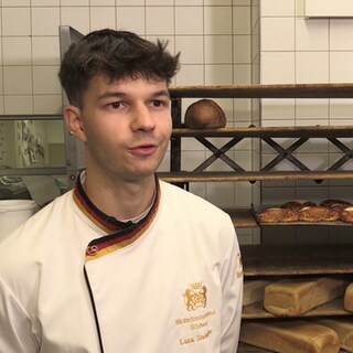 Brezelkönig Luca Stadelhofer steht in der Bäckerei und spricht in die Kamera.