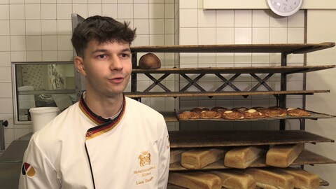 Brezelkönig Luca Stadelhofer steht in der Bäckerei und spricht in die Kamera.