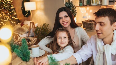 Eine junge Familie sitzt gemütlich und zufriedend lächelnd an einem Tisch inmitten von Weihnachtsdekoration