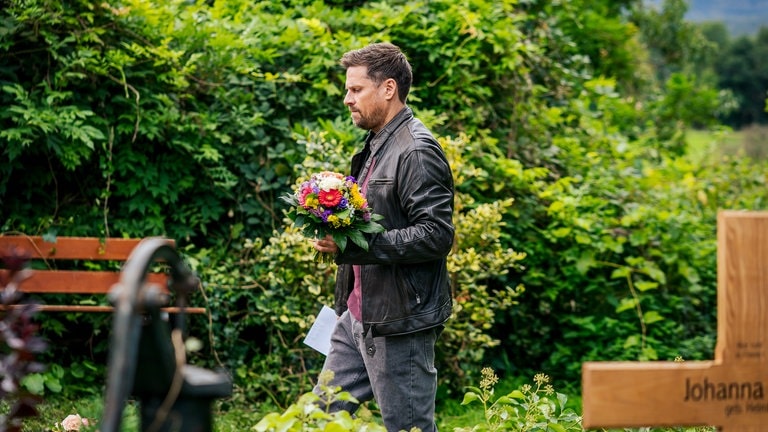 Andreas (Ralph Gassmann) läuft mit Blumen in der Hand über den Friedhof