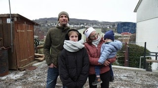 Familie Böhler steht frontal vor dem Grundstück ihres durch einen Großbrand zerstörten Hauses.