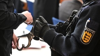 Symbolbild: Ein Justizvollzugsbeamter nimmt einem Angeklagten Handschellen ab. Vor dem Landgericht Konstanz beginnt am Montag ein Prozess gehen drei Männer, die mehrere junge Frauen zur Prostitution gezwungen haben sollen.