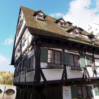 Das Schiefe Haus in Ulm. Ein altes Fachwerkhaus kippt leicht nach links. In der Mitte ist die Aufschrift "Schiefes Haus" auf dem Gebäude zu sehen.