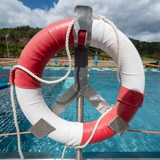 Ein Rettungsreifen hängt auf einem Geländer, vor einem Schwimmbecken.