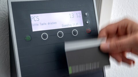 Symbolbild | Eine Hand fährt mit Bewegungsunschärfe an einem Gerät zur digitalen Zeiterfassung entlang: Ein Mitarbeiter erfasst seine Arbeitszeit digital an einem Terminal. 