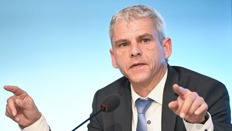 Ein Mann an einem Mikrofon zeigt mit beiden Fingern.