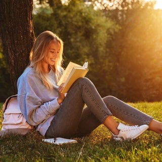 Frau liest bei Sonnenuntergang ein Buch und lächelt