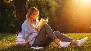 Frau liest bei Sonnenuntergang ein Buch und lächelt