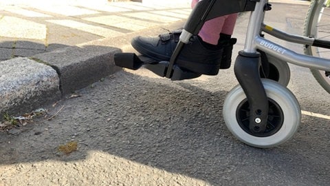 Ein Rollstuhlfahrer aus Kusel im Kreis Kaiserslautern steht vor einem hohen Bürgersteig.