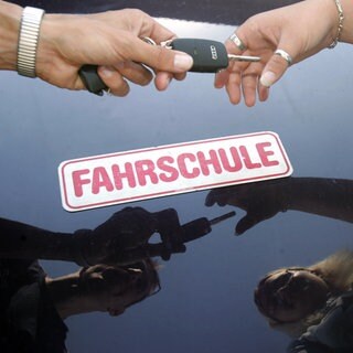 Ein Fahrlehrer überreicht seiner Fahrschülerin den Schlüssel zum Fahrzeug (Symbol): In einer Fahrschule in Brackenheim sollen falsche, bezahlte Prüflinge die Theorieprüfung absolviert haben.