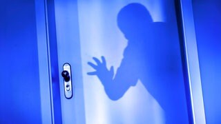 Ein Einbrecher will im Schutz der Dunkelheit eine Wohnungstür aufbrechen.