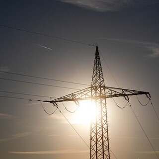 Ein Strommast wird von der Sonne angestrahlt. Verursachen hohe Temperaturen Stromausfälle?