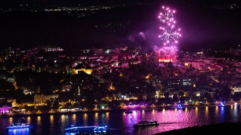 Schiffe fahren auf dem Rhein vor Bingen, im Hintergrund Feuerwerk. Entlang der schönsten Rheinabschnitte finden die Feuerwerksspektakel Rhein in Flammen statt. Bingen und Rüdesheim bilden den Auftakt.