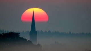 Die Silhouette eines Kirchturms vor der aufgehenden Sonne