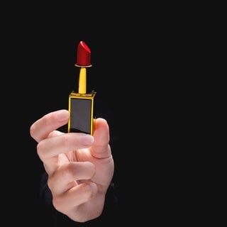 Red lipstick in a woman's hand on a dark background. Symbolfoto.