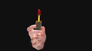 Red lipstick in a woman's hand on a dark background. Symbolfoto.