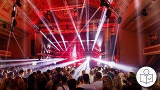 Menschen bei einem Konzert im Kurhaus Baden-Baden. Viele weiße Lichter sind im Raum. Das Konzert ist beim New Pop Festival. Rechts das SWR Logo für Leichte Sprache.