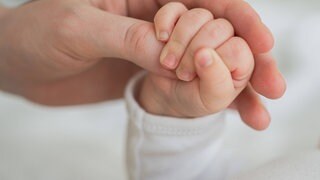 Symbolbild: Die Hand eines Neugeborenen umfasst den Daumen der Mutter.