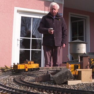 Ulrich Höflacher steht in seinem Garten und bedeint seine Modelleisenbahn.