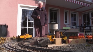 Ulrich Höflacher steht in seinem Garten und bedeint seine Modelleisenbahn.