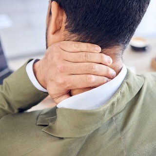 Mann fasst sich mit der Hand ins Genick. Zu den häufigsten gesundheitlichen Beschwerden gehören Nackenschmerzen. Was gegen Muskelverspannung, Fehlhaltung oder chronischen Schmerz hilft: von Physiotherapie über Kraftübungen bis Akupunktur.