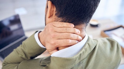 Mann fasst sich mit der Hand ins Genick. Zu den häufigsten gesundheitlichen Beschwerden gehören Nackenschmerzen. Was gegen Muskelverspannung, Fehlhaltung oder chronischen Schmerz hilft: von Physiotherapie über Kraftübungen bis Akupunktur.