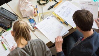 Eine Schülerin und ein Schüler lösen eine Matheaufgabe. Unangemeldete Hausaufgabenprüfungen fallen in RLP künftig weg.
