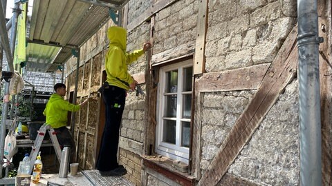 Zwei junge Handwerker arbeiten an der Außenfassade eines alten Fachwerkhauses, dass bei der Flut 2021 zerstört wurde.