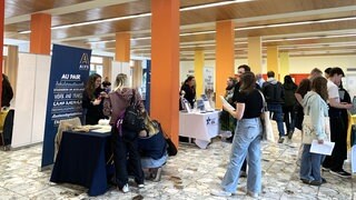 In einem Schulgebäude in Freiburg sind Infostände aufgebaut zu Auslandsaufenthalten für junge Menschen. Viele Jugendliche informieren sich mit ihren Eltern auf der Jugendbildungsmesse. Die USA ist ein beliebtes Zielland für Schulaufenthalte, aber durch Trump ändern sich einige Dinge.