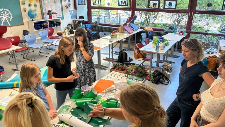 Schülerinnen und Lehrerinnen stehen an einem Tisch mit Bastelmaterialien. Schüler des Carlo-Schmid-Gymnasiums in Tübingen übernehmen die Gestaltung ihrer Schultioletten selbst.