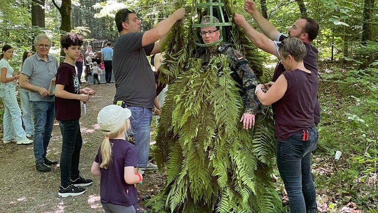 "Pfingstträg" Philipp Weber wird vor Ort im Wald von allen zusammen eingekleidet. Ein Eisengestell soll sein Gesicht schützen.