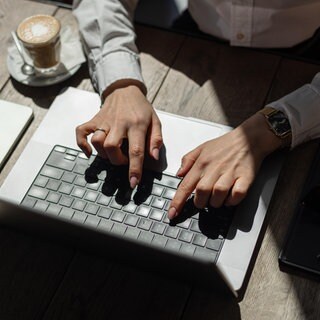 Junge Frau tippt auf einem Laptop an einem Cafétisch: Bei der Mainzer und Wormser Gründungswoche bekommen Interessierte ab dem 17. November einen ersten Einblick in Gründungsthemen.